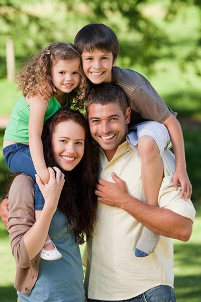 A family of four smiling in a forest as they hug
